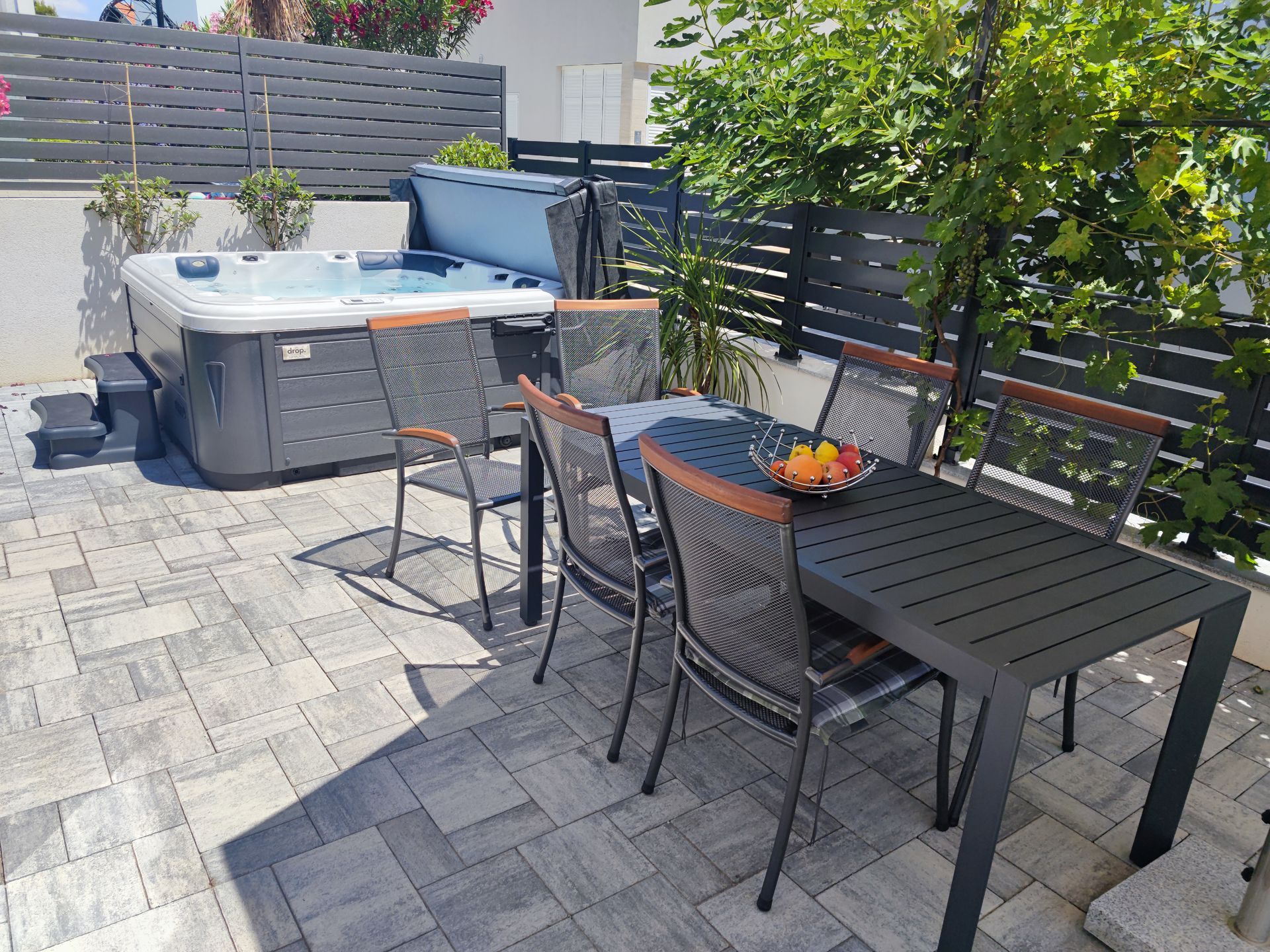 Patio with hot tub, table and chairs, gray pavers, fenced.