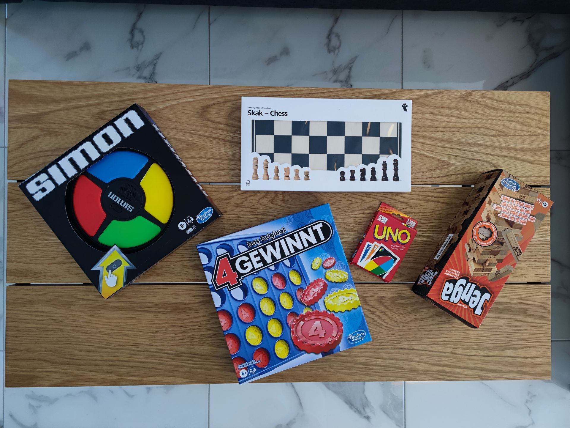 Board games arranged on a wooden surface: Simon, chess set, Gewinnt, Uno, and Jenga.