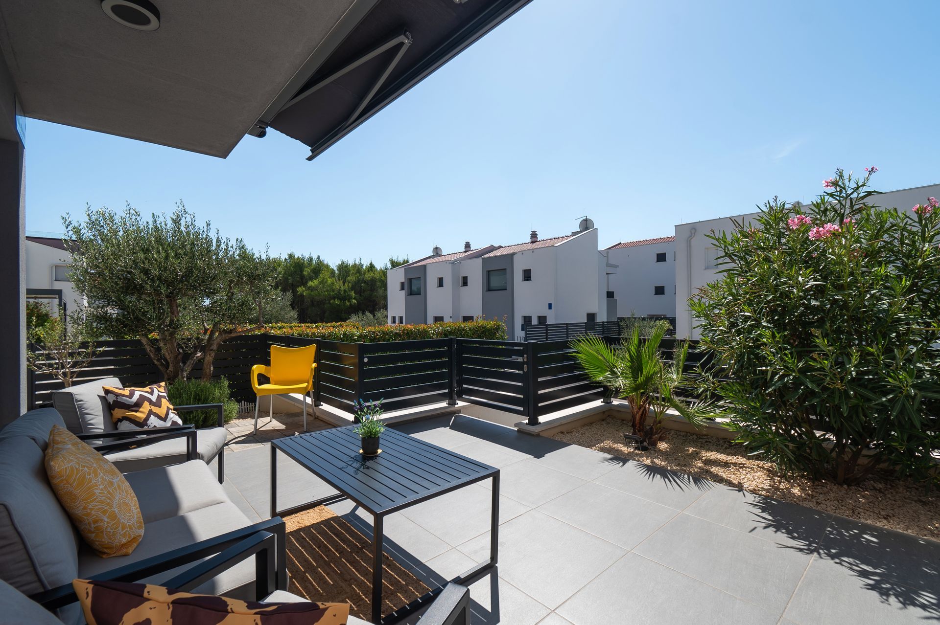 Patio with gray furniture, black table, yellow chair, and a view of townhouses.