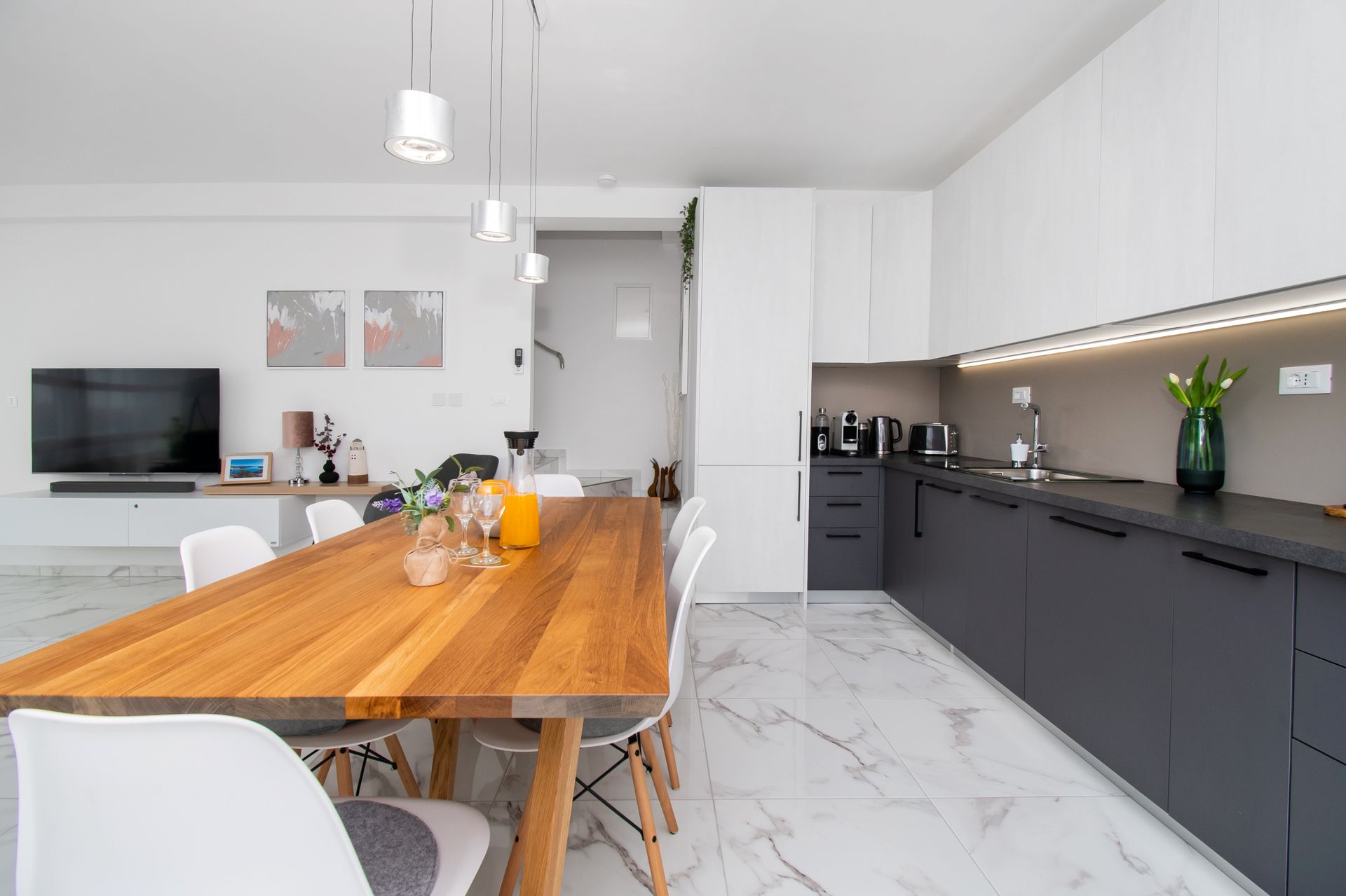 Modern kitchen and dining area with wooden table, white chairs, and gray and white cabinetry.