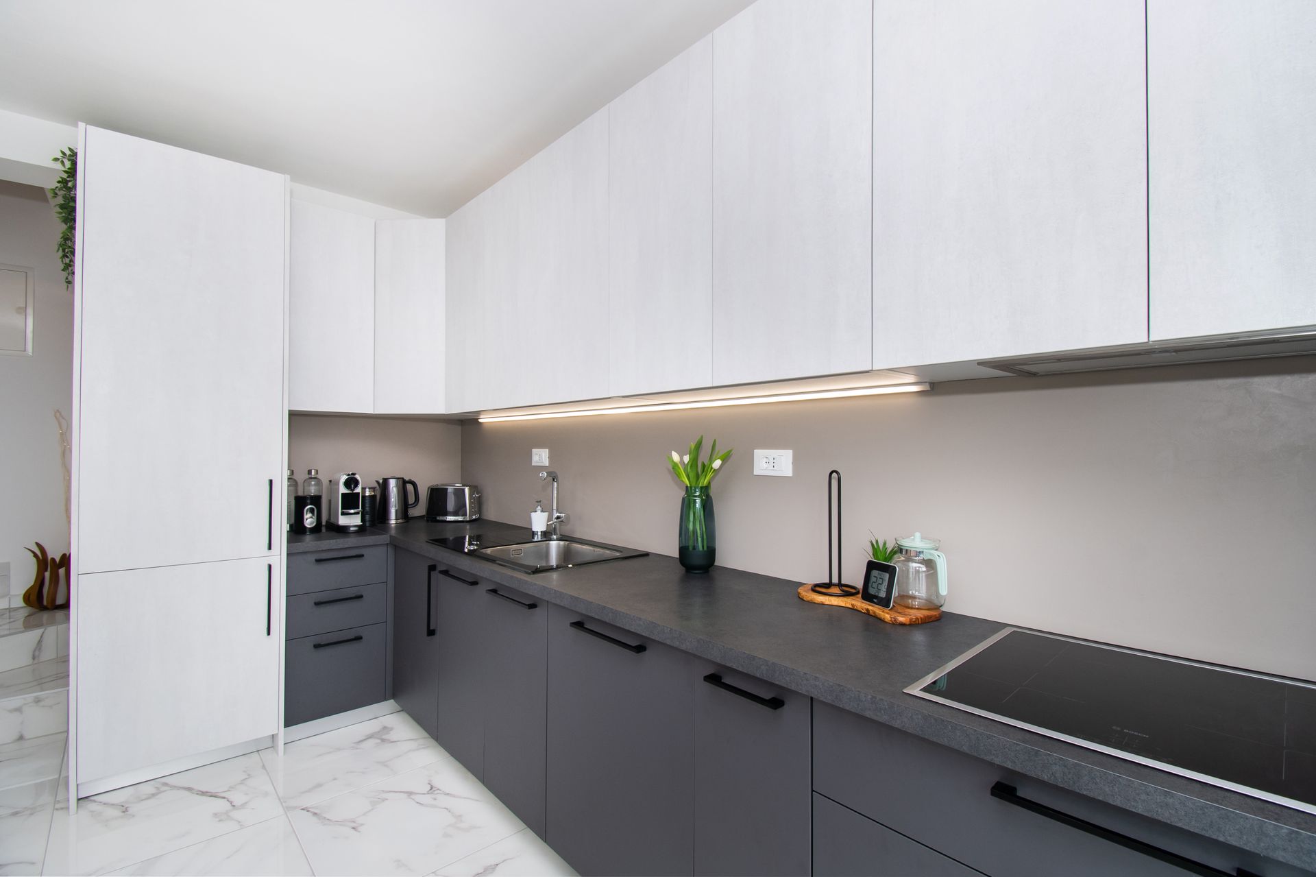 Modern kitchen with gray and white cabinets, black countertops, and a stovetop.