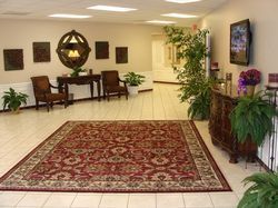 Lobby with red patterned rug, chairs, plants, and art. Neutral tones with a welcoming aesthetic.