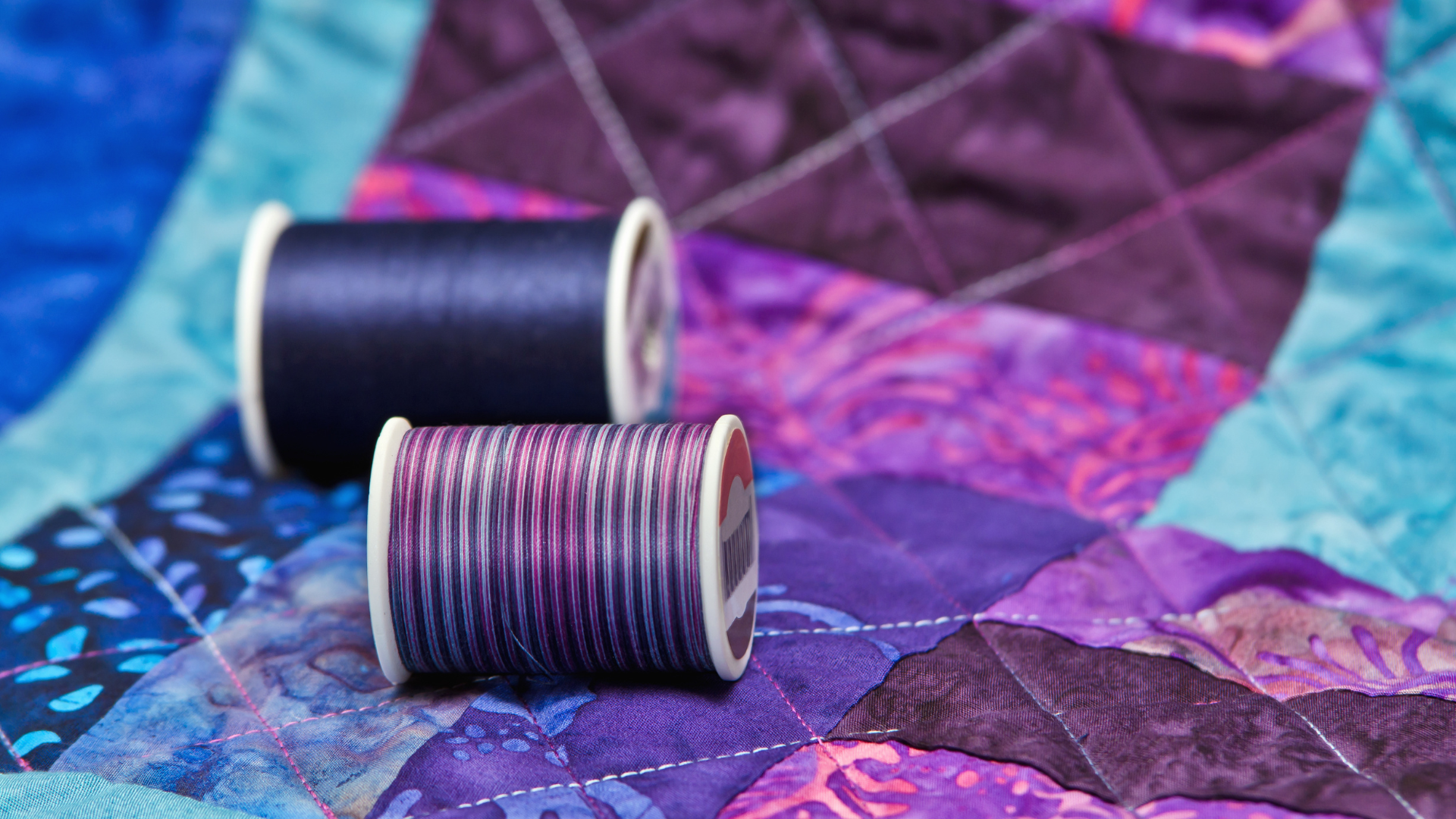 Three spools of thread are sitting on top of a quilt.