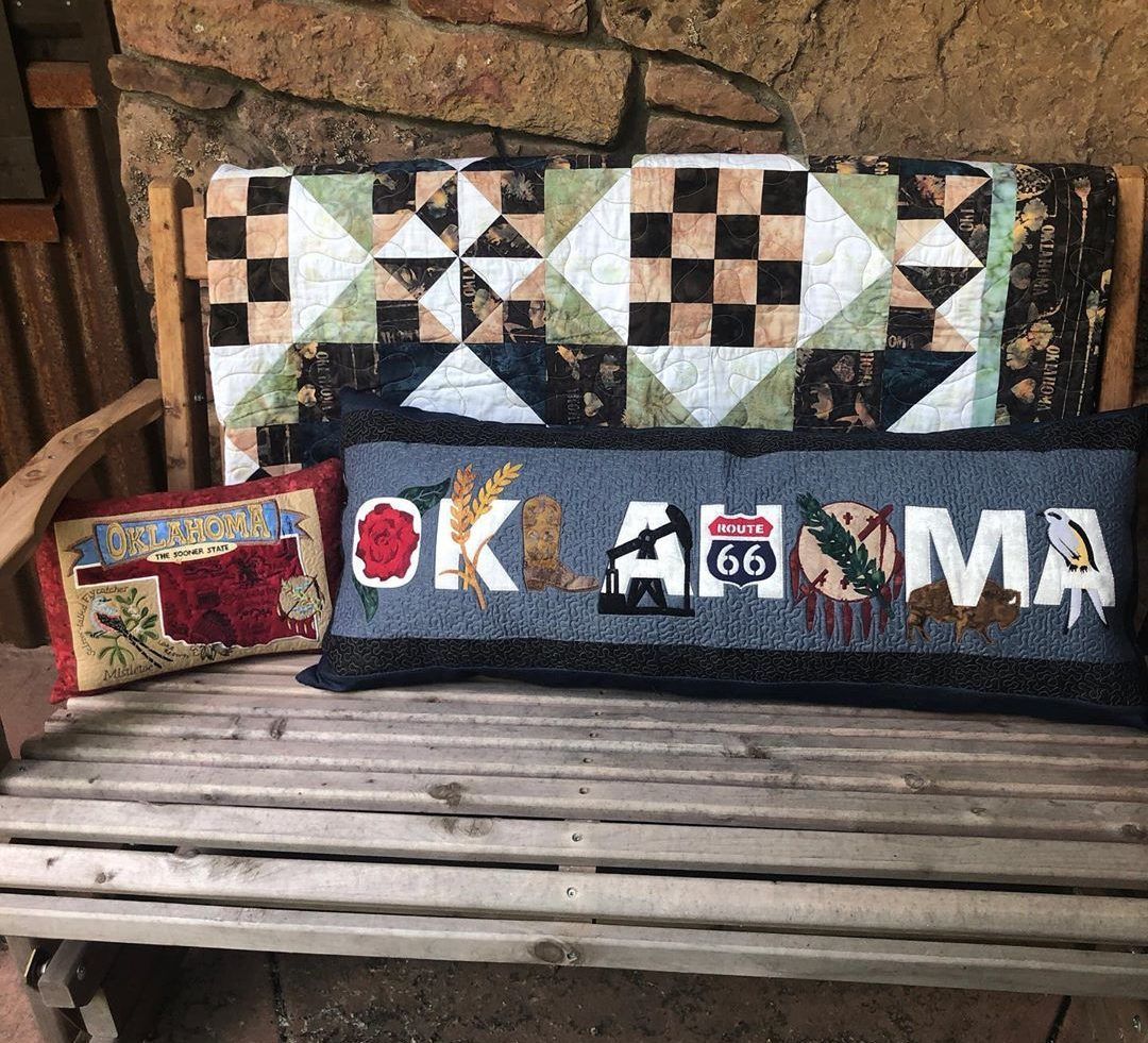 A wooden bench with a quilt and two pillows on it.