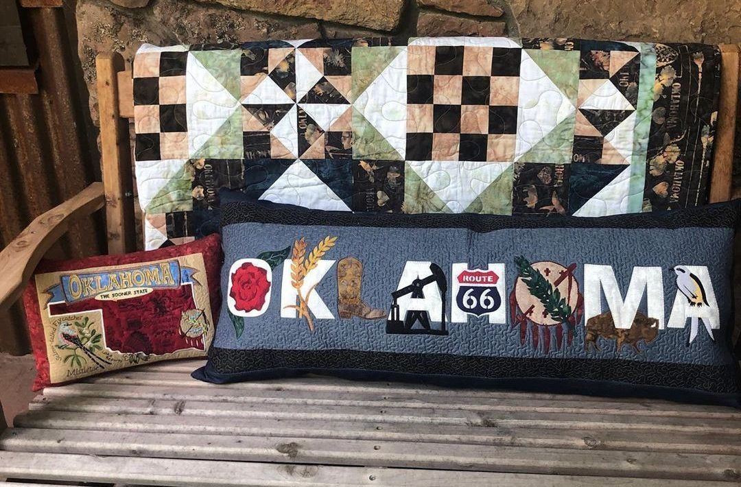 A wooden bench with a quilt and two pillows on it.