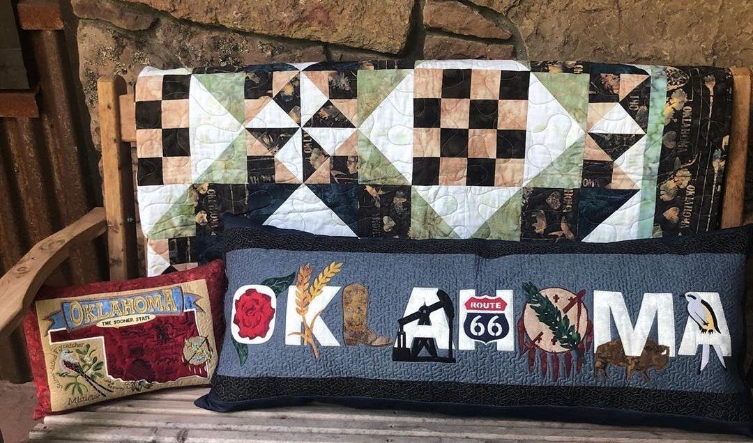 A quilt and two pillows are sitting on a wooden bench.