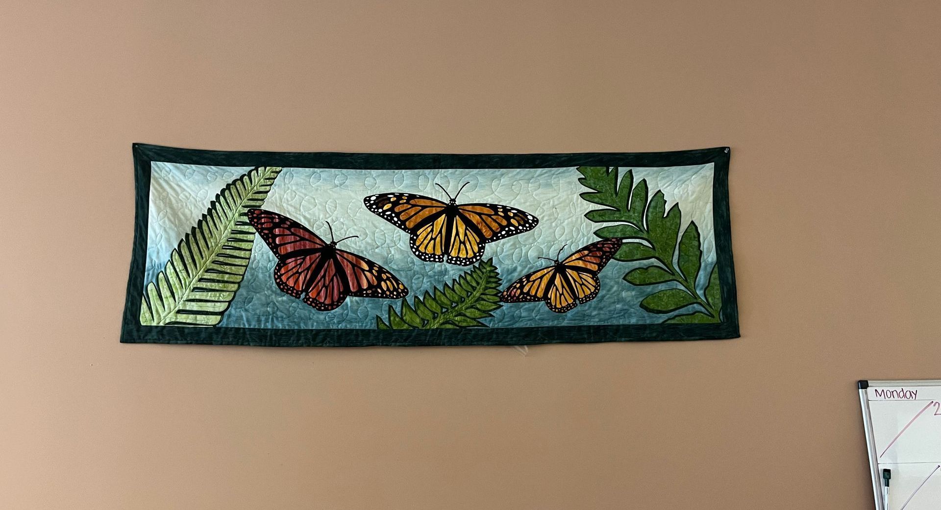 A painting of three butterflies and ferns is hanging on a wall.