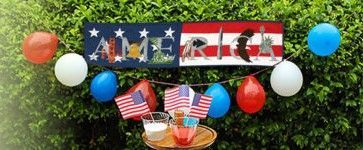 A sign that says `` america '' is hanging on a bush with balloons and flags.