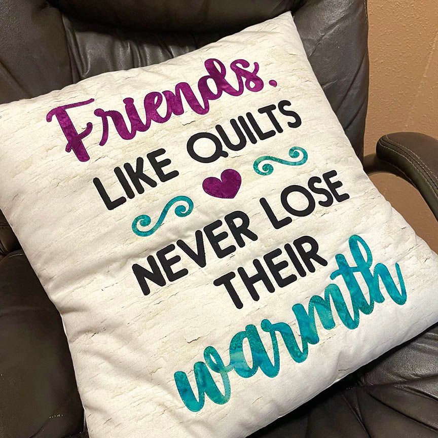 A pillow that says `` friends like quilts never lose their warmth '' is sitting on a chair.