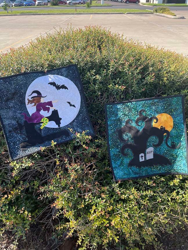 Two halloween quilts are sitting on top of a bush.