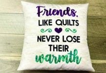 A pillow that says `` friends like quilts never lose their warmth '' is sitting on a wooden table.