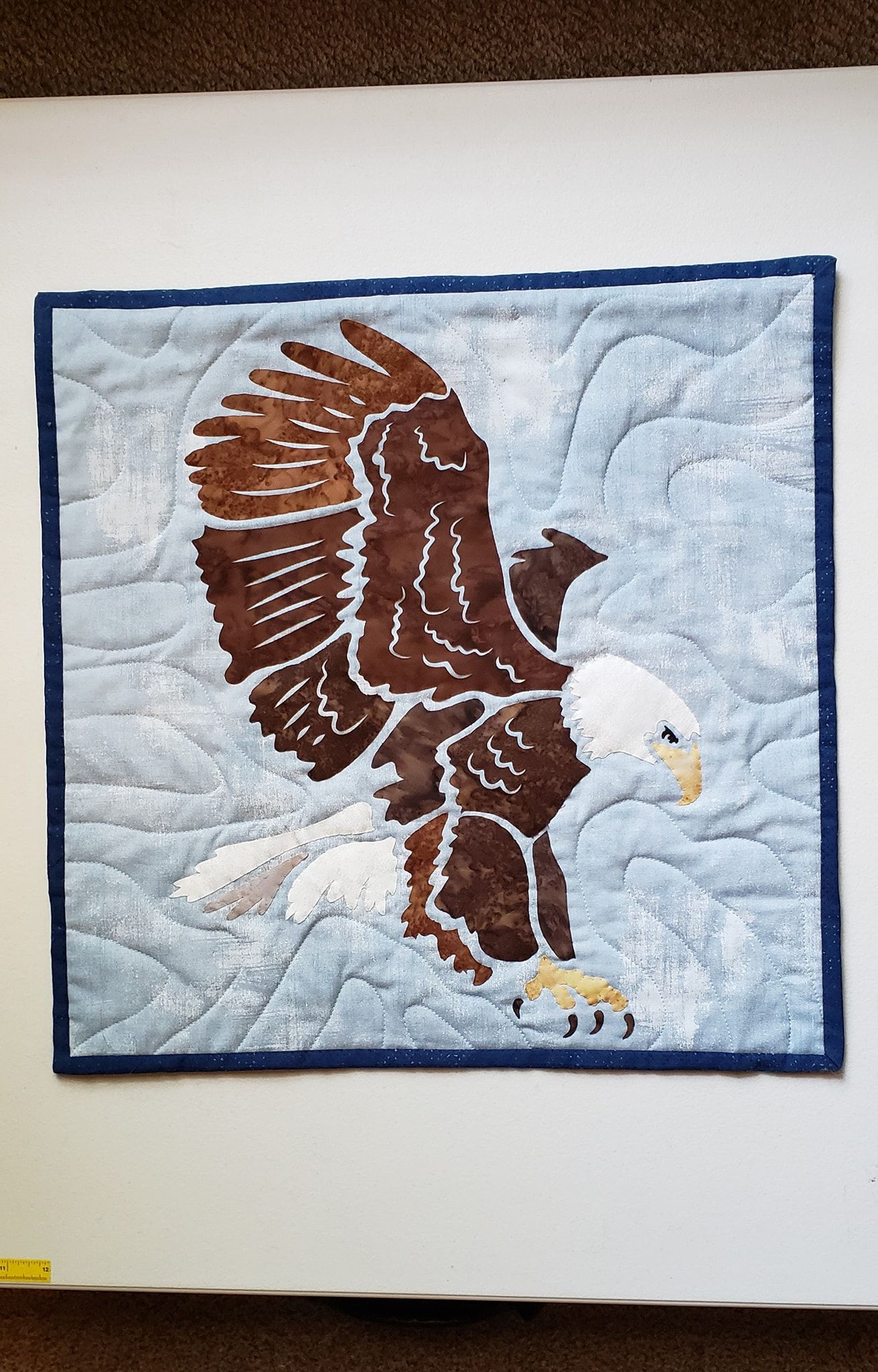 A quilt of a bald eagle flying over a snowy field.