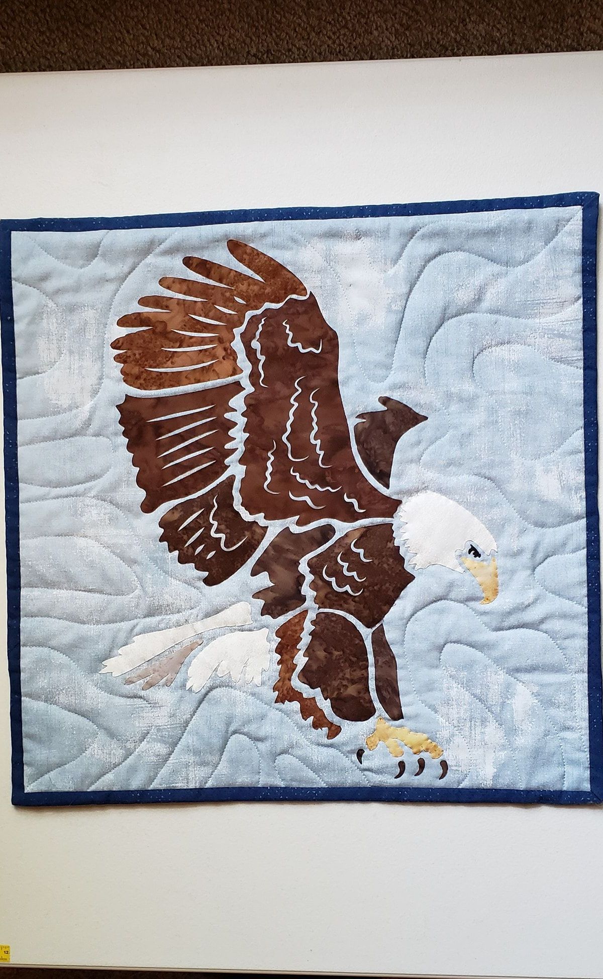 A quilt of a bald eagle flying over a snowy field.