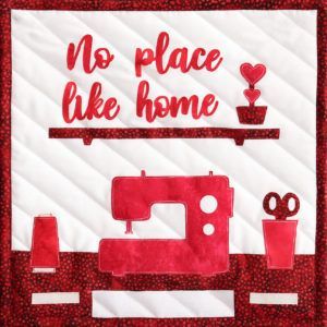 A quilt with a sewing machine and scissors that says no place like home