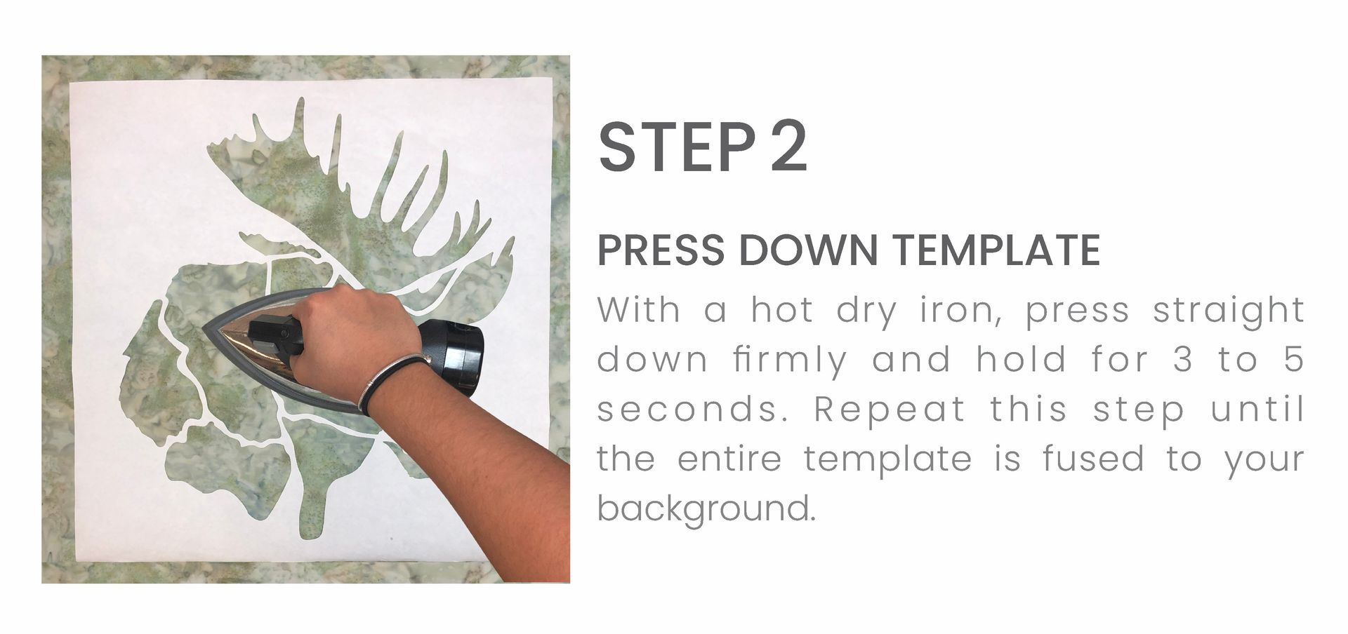 A person is ironing a picture of a moose on a piece of fabric.