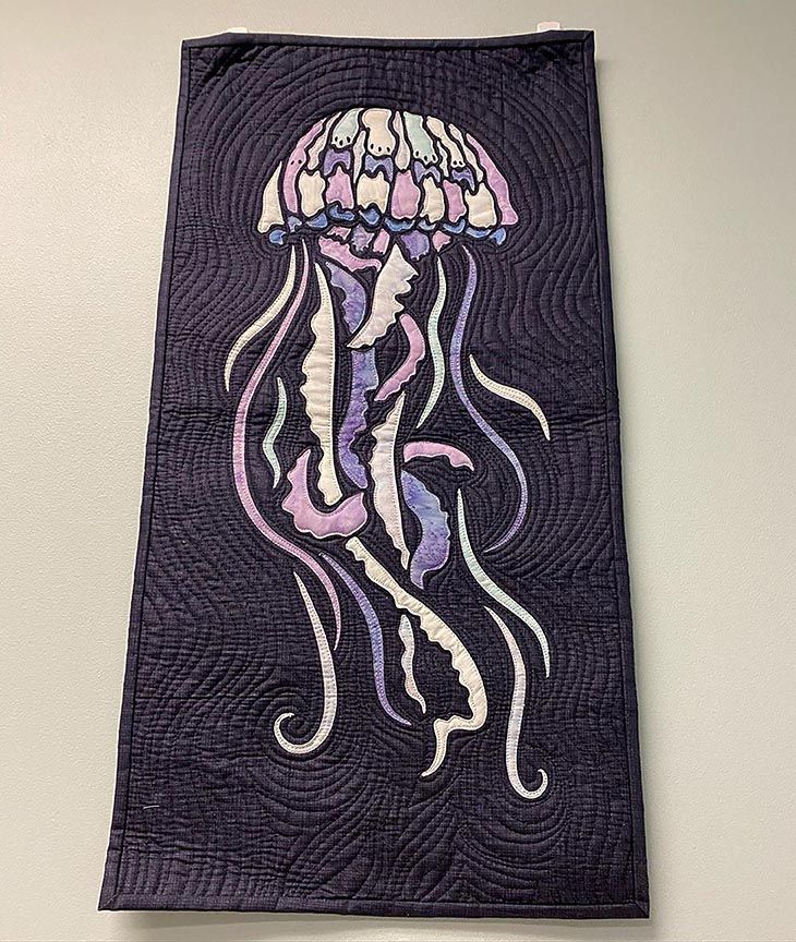 A quilt with a jellyfish on it is hanging on a wall.