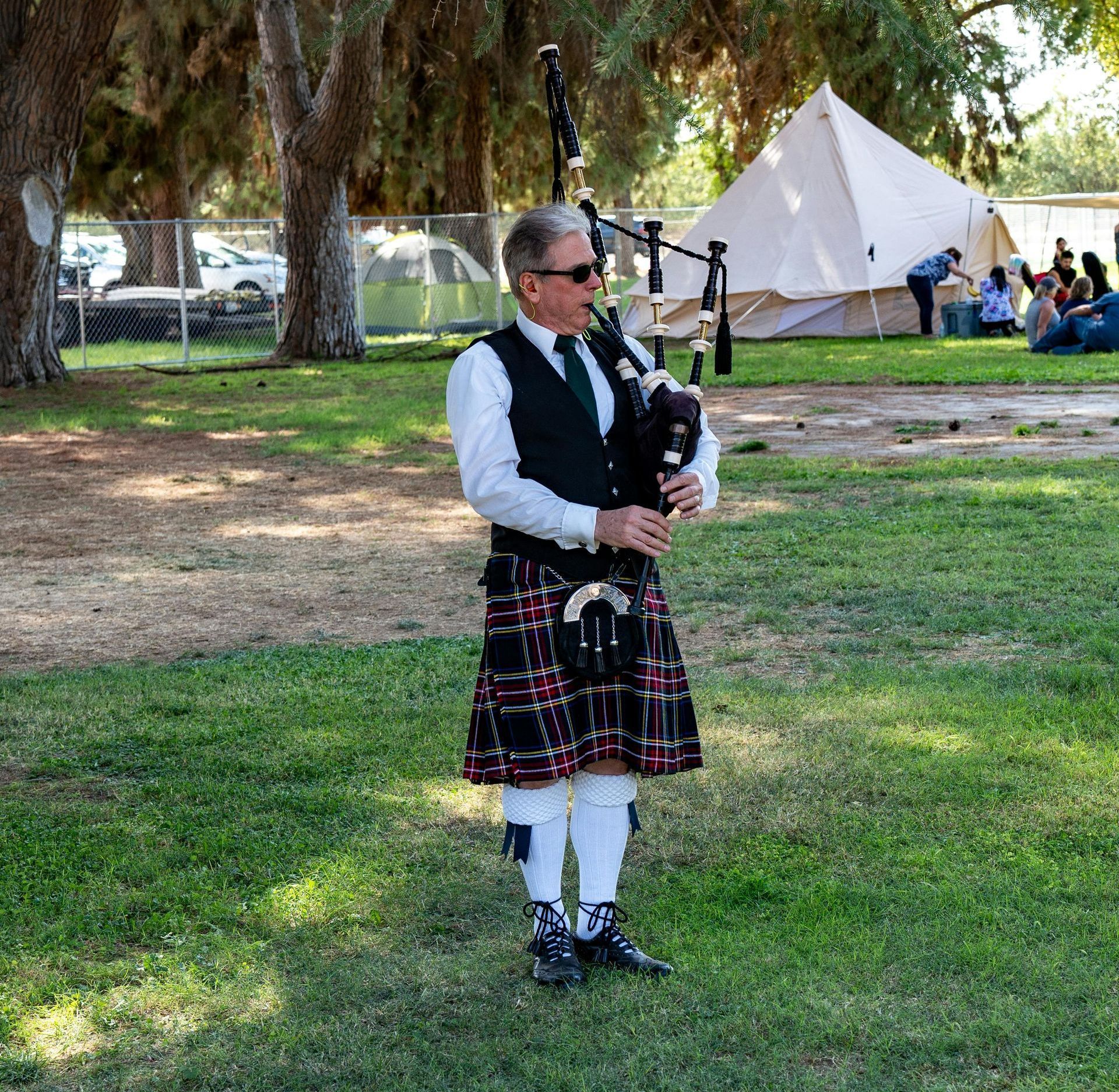 A man in a kilt is playing a bagpipe in a park