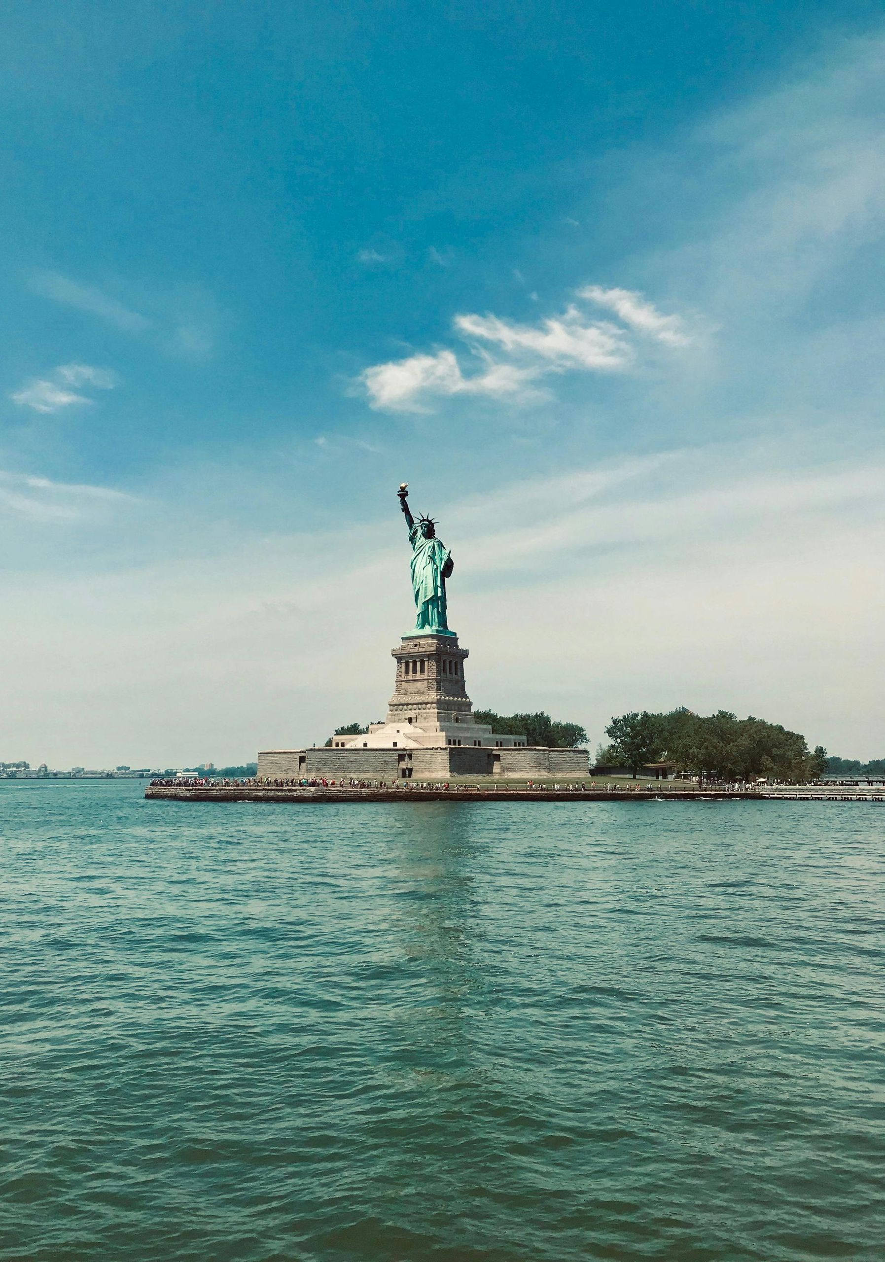 The statue of liberty is sitting on a small island in the middle of the ocean.