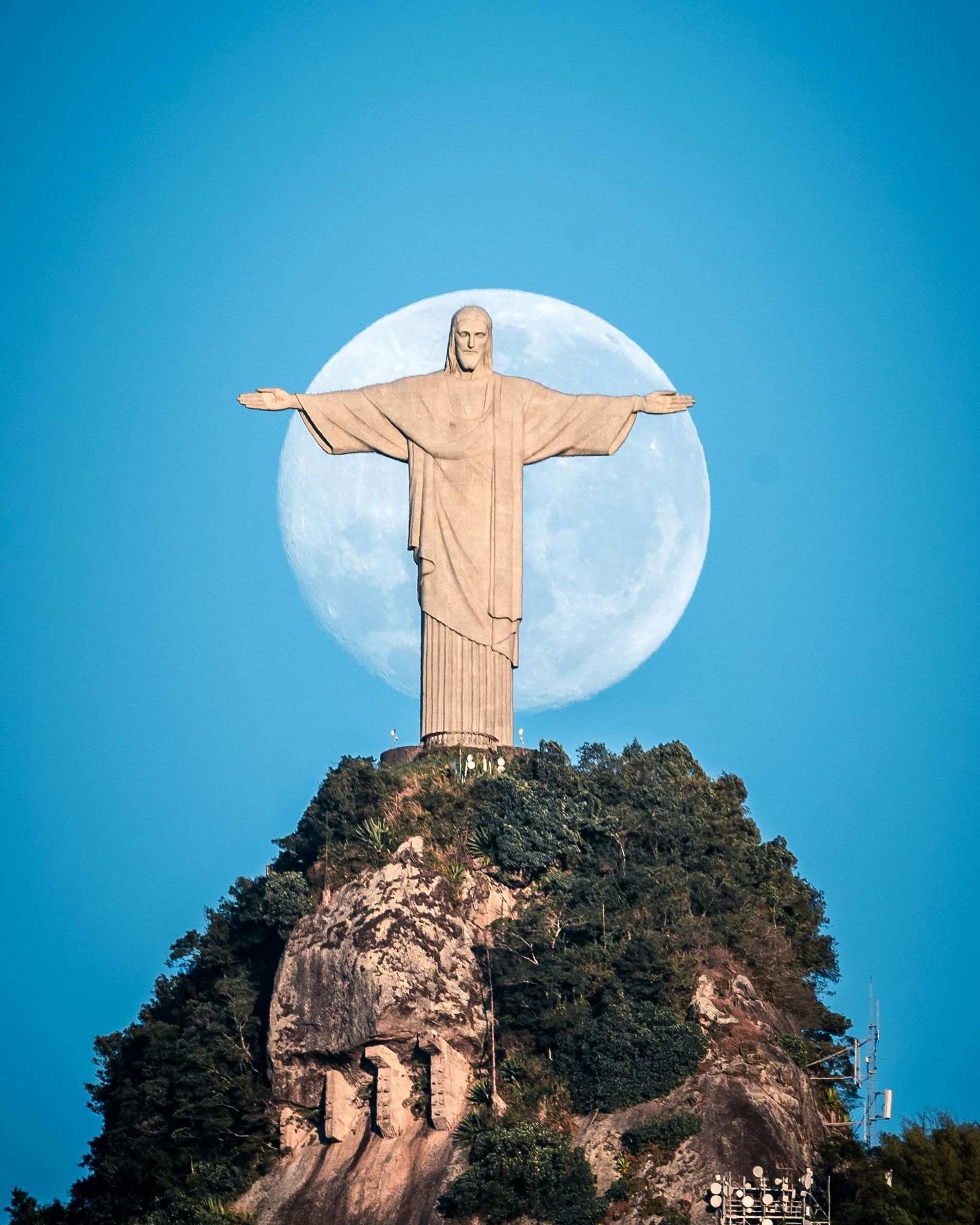 A statue of jesus on top of a hill with a full moon in the background.