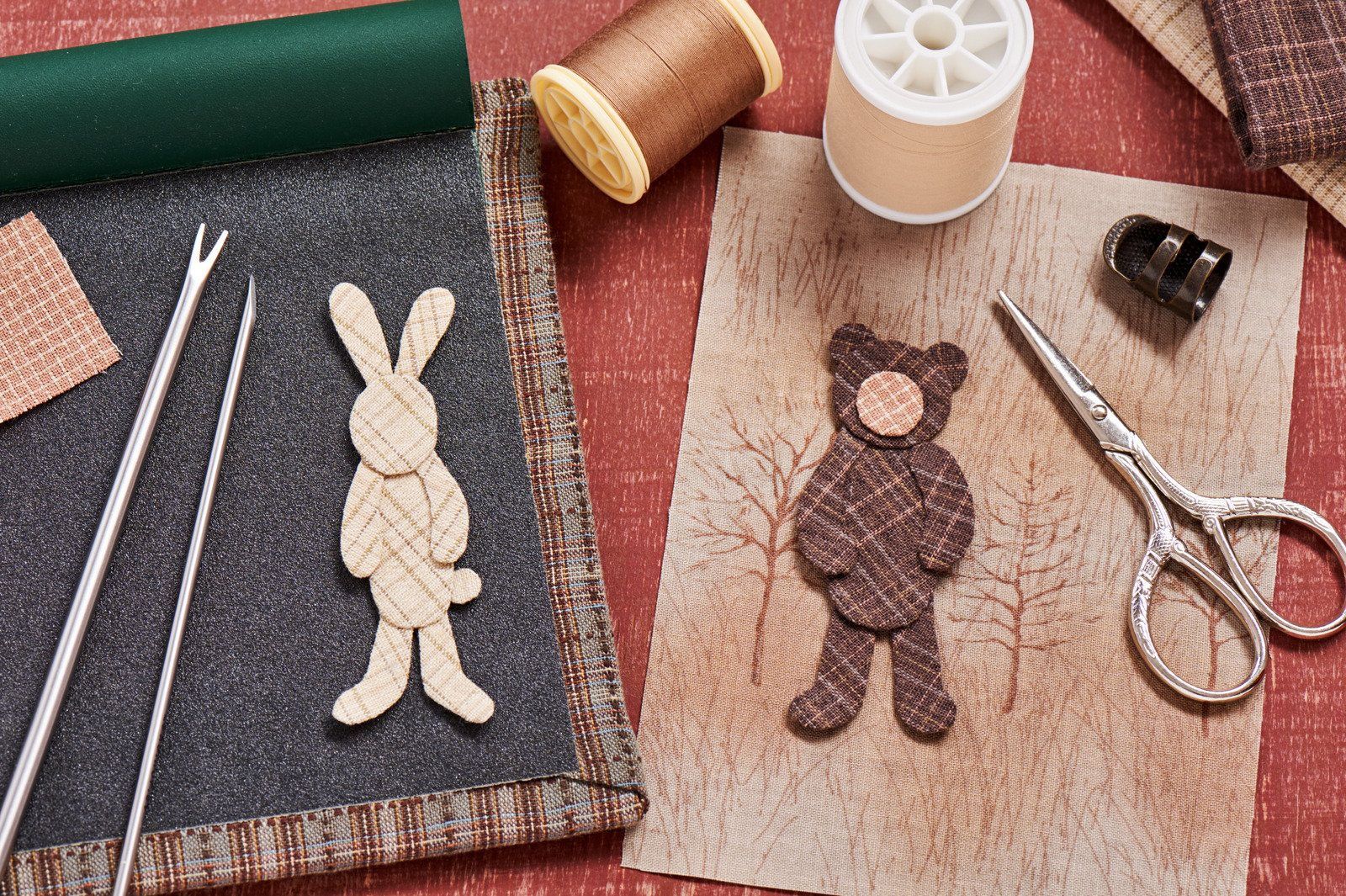 A rabbit and a teddy bear are sitting on a table with sewing supplies.