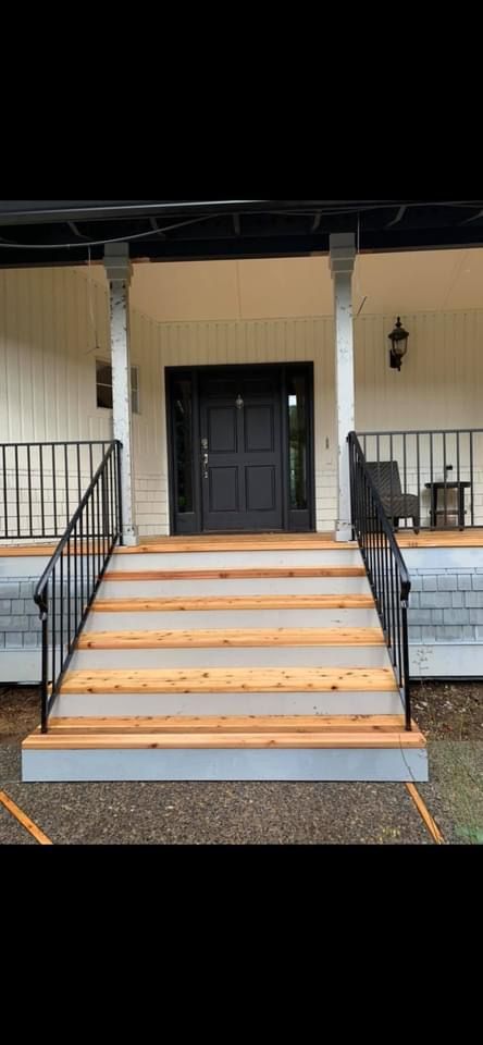 The front porch of a house with wooden steps and a black door.
