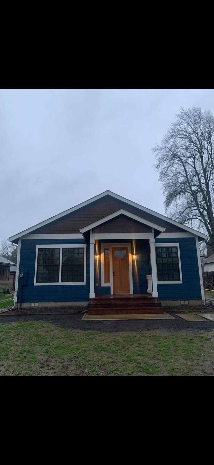 A blue house with a brown roof and a wooden door is for sale.