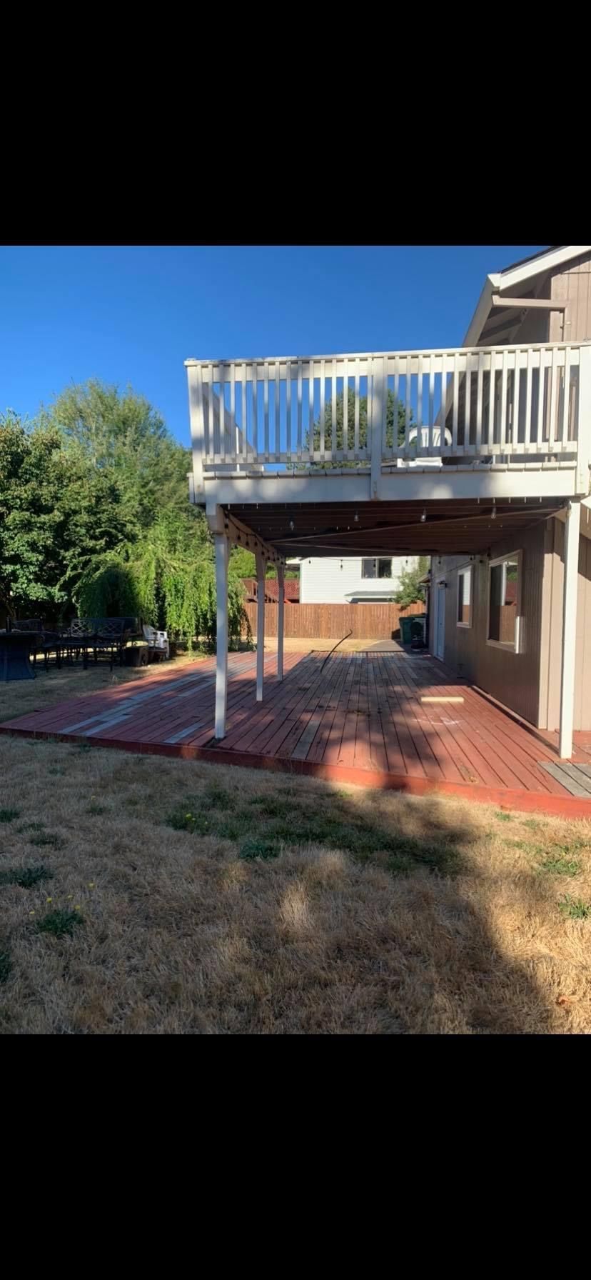 A large deck with a white railing is sitting underneath a house.