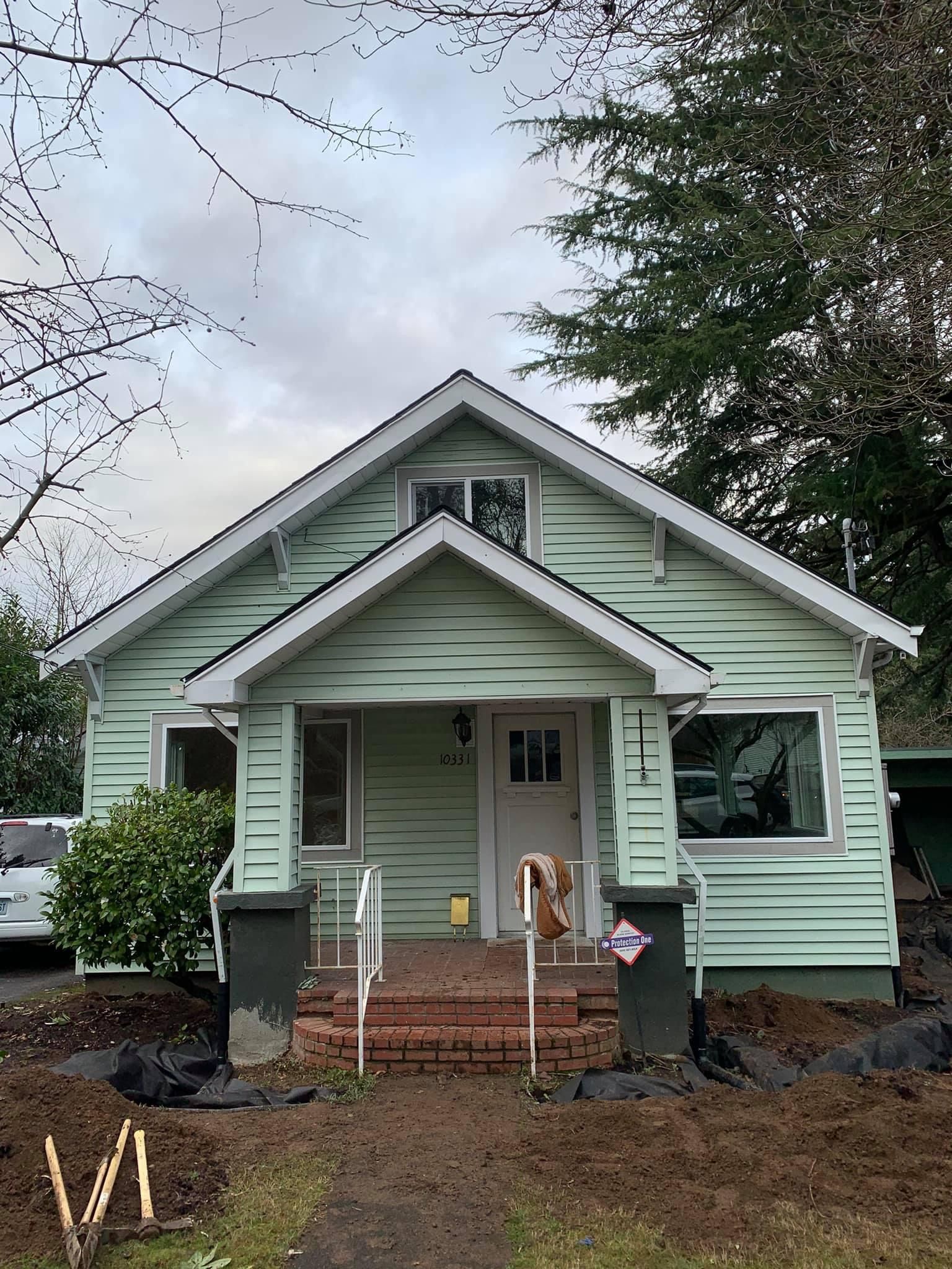 A small green house with a dog on the porch.