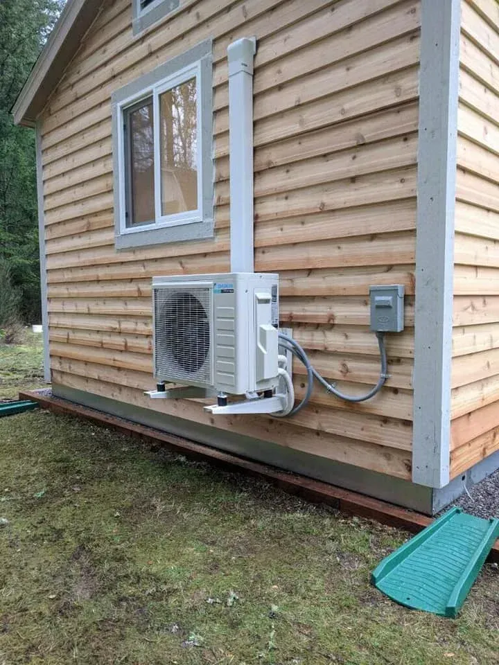 An air conditioning unit mounted on the wooden exterior of a small building.