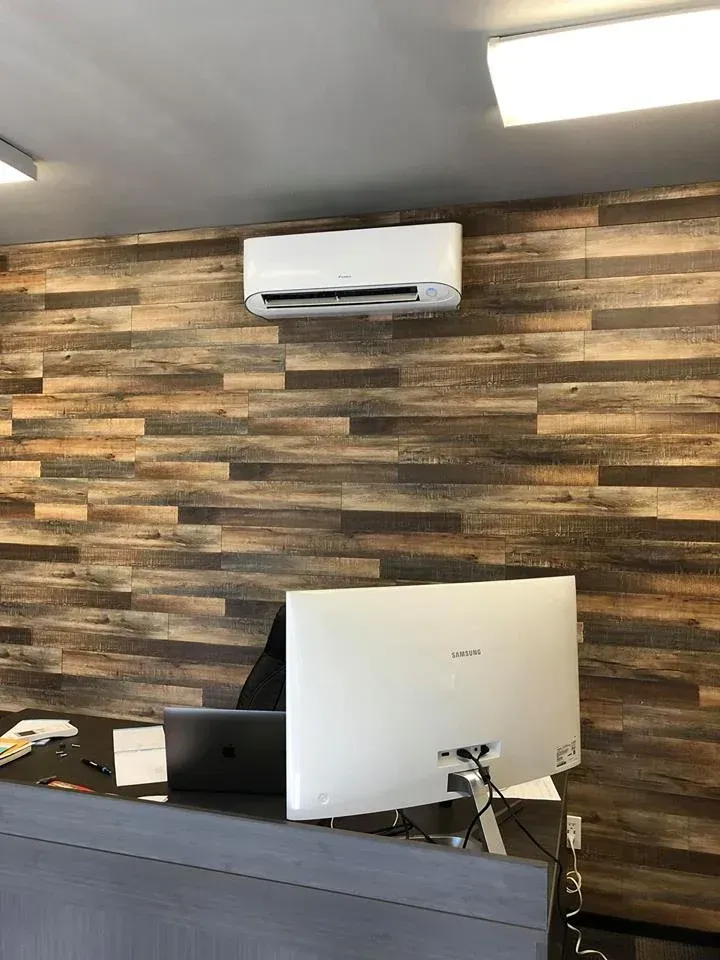 Air conditioning unit mounted on a wood-paneled wall above a desk with a computer monitor.