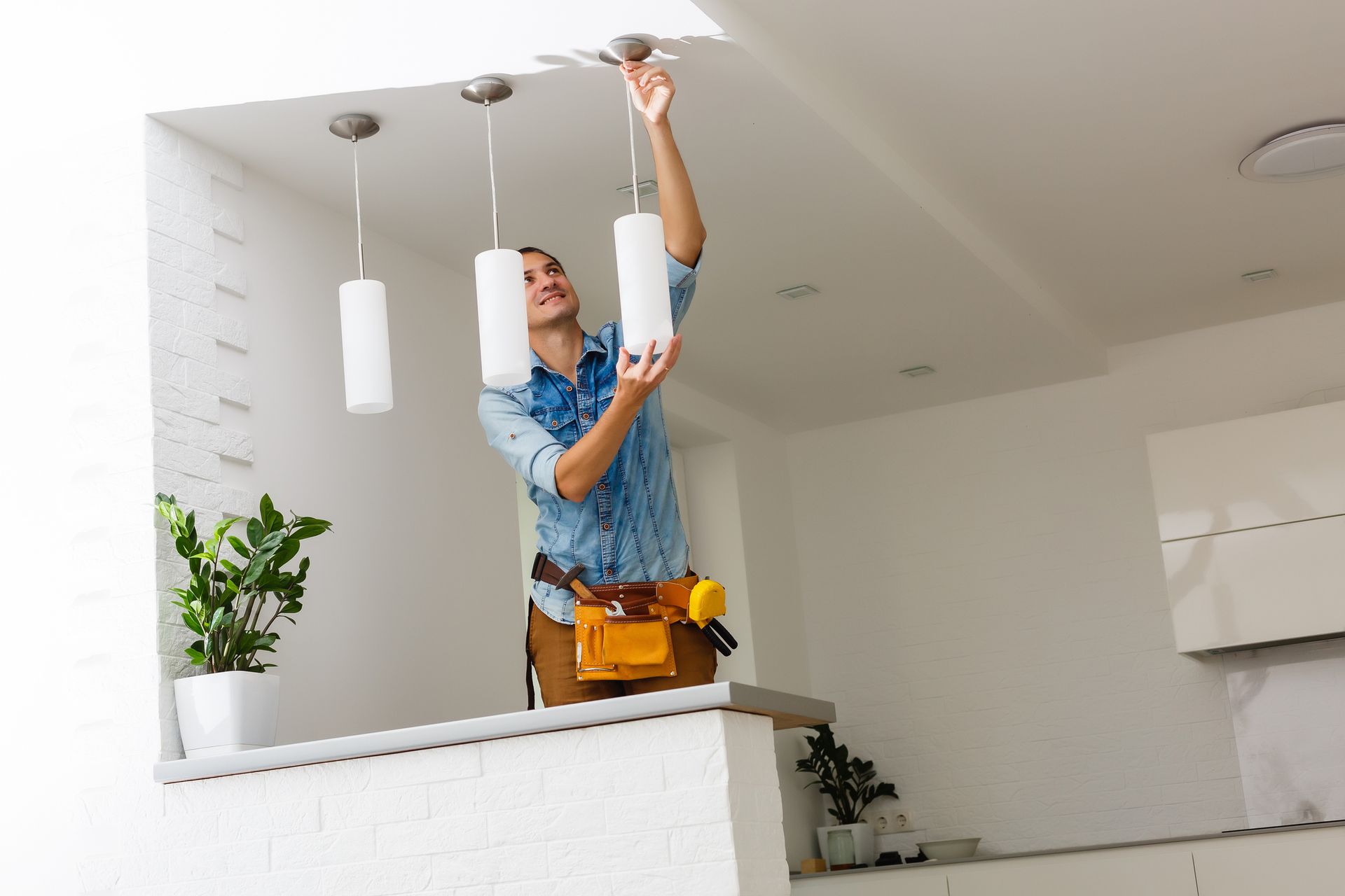 Man installing a pendant light, smiling, in a white room.