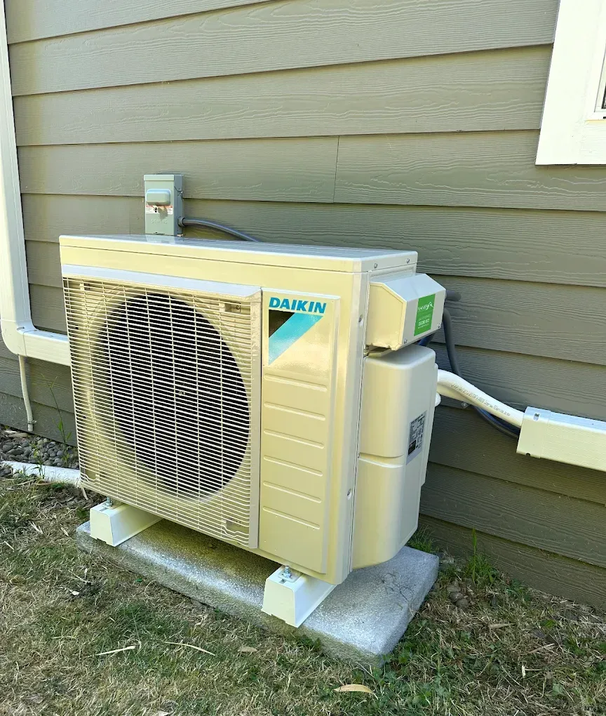 Daikin air conditioning unit mounted on a concrete slab outside a building with gray siding.