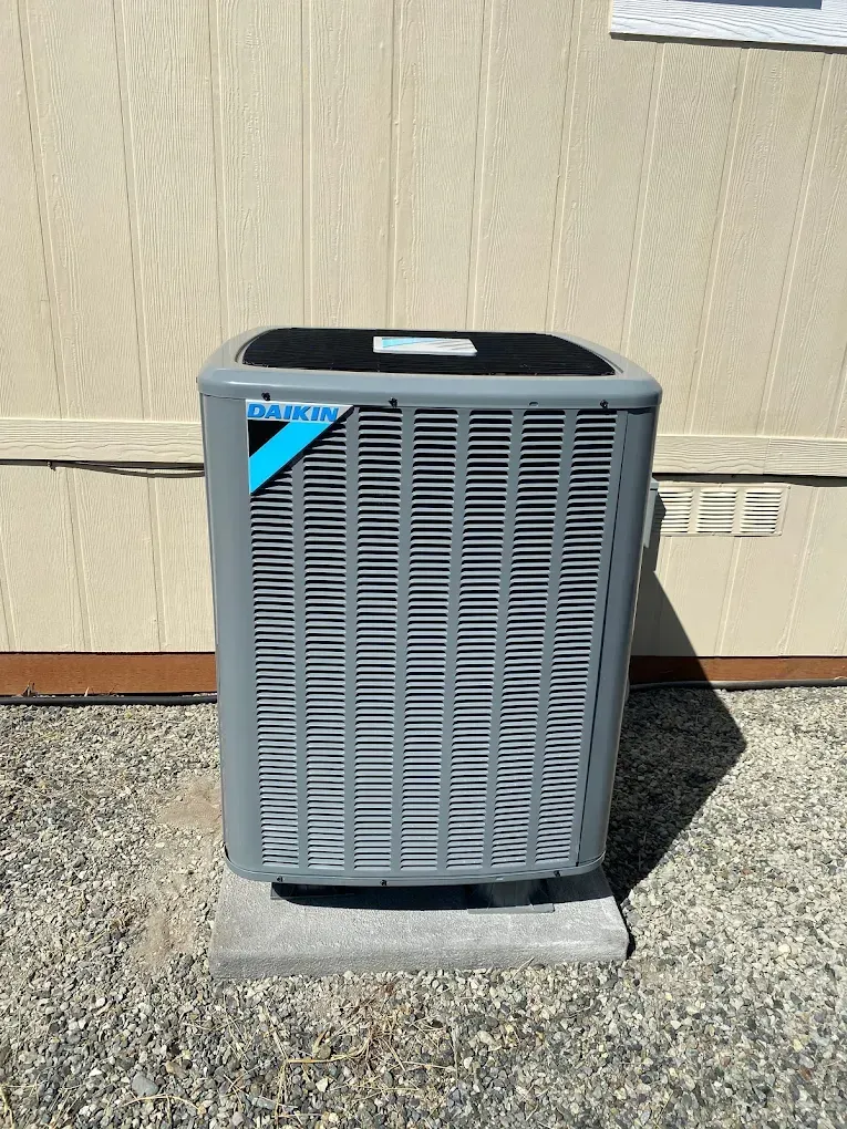 Daikin air conditioning unit outside on a concrete base, against a beige wall.