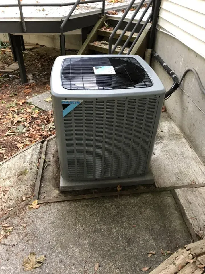 An outdoor Daikin air conditioning unit sits on a concrete pad next to a house.