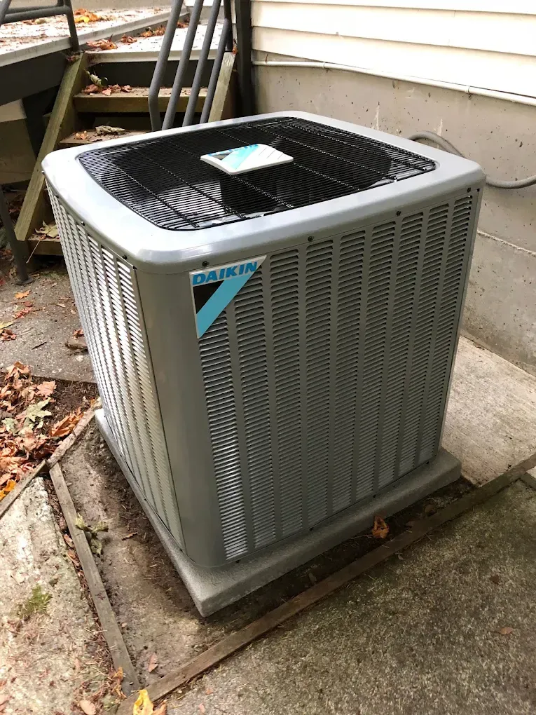 Daikin air conditioner unit outside a building, gray with a black top, on a concrete pad.