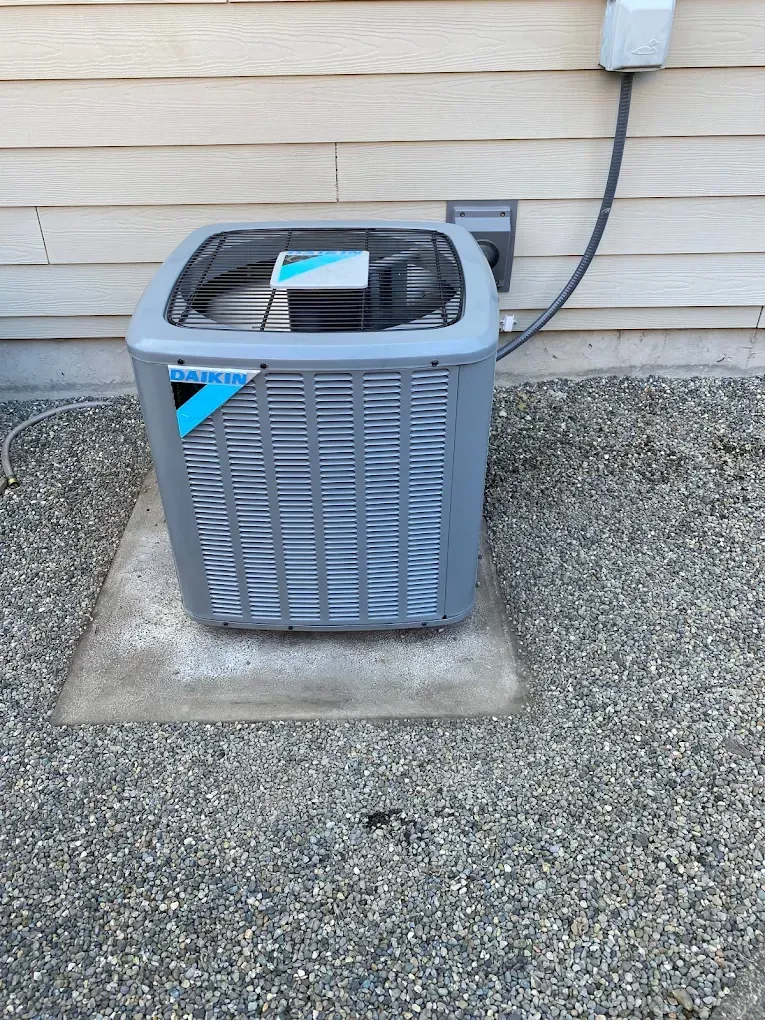Daikin air conditioning unit outside a building, on a concrete pad, gravel ground.