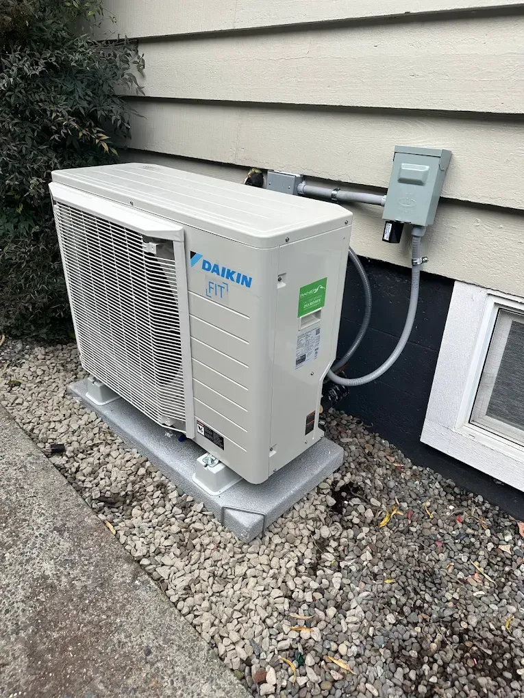 Daikin heat pump unit on a concrete pad next to a building, with electrical conduit and a small window.