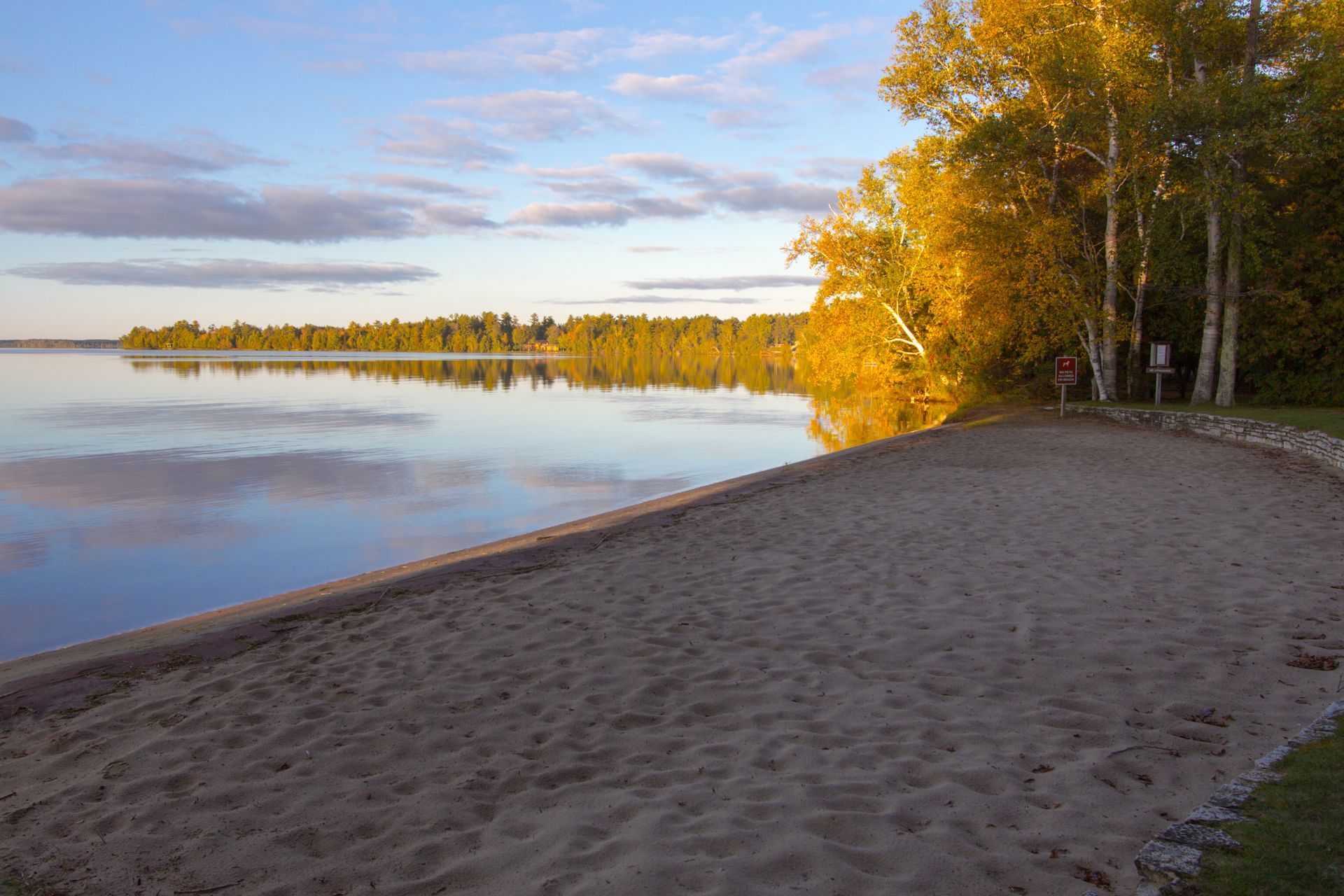 a sandy beach next to a lake with trees in the background .