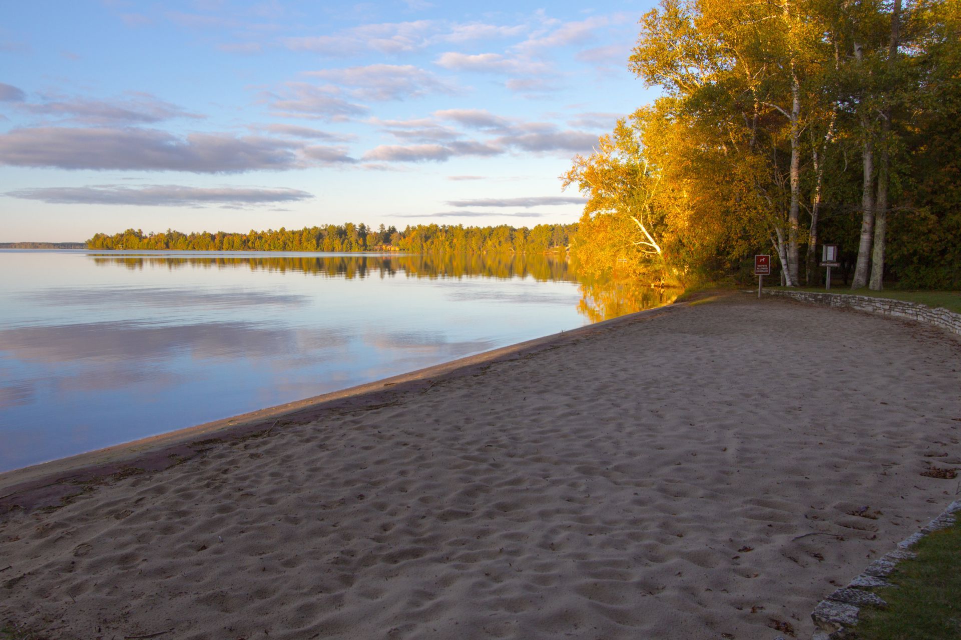 A sandy beach next to a lake with trees in the background.