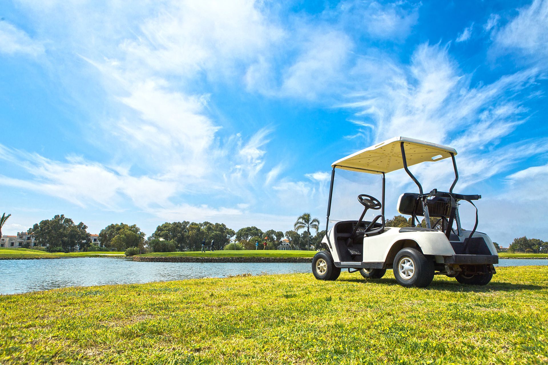 A golf cart is parked on the grass next to a body of water on a golf course.