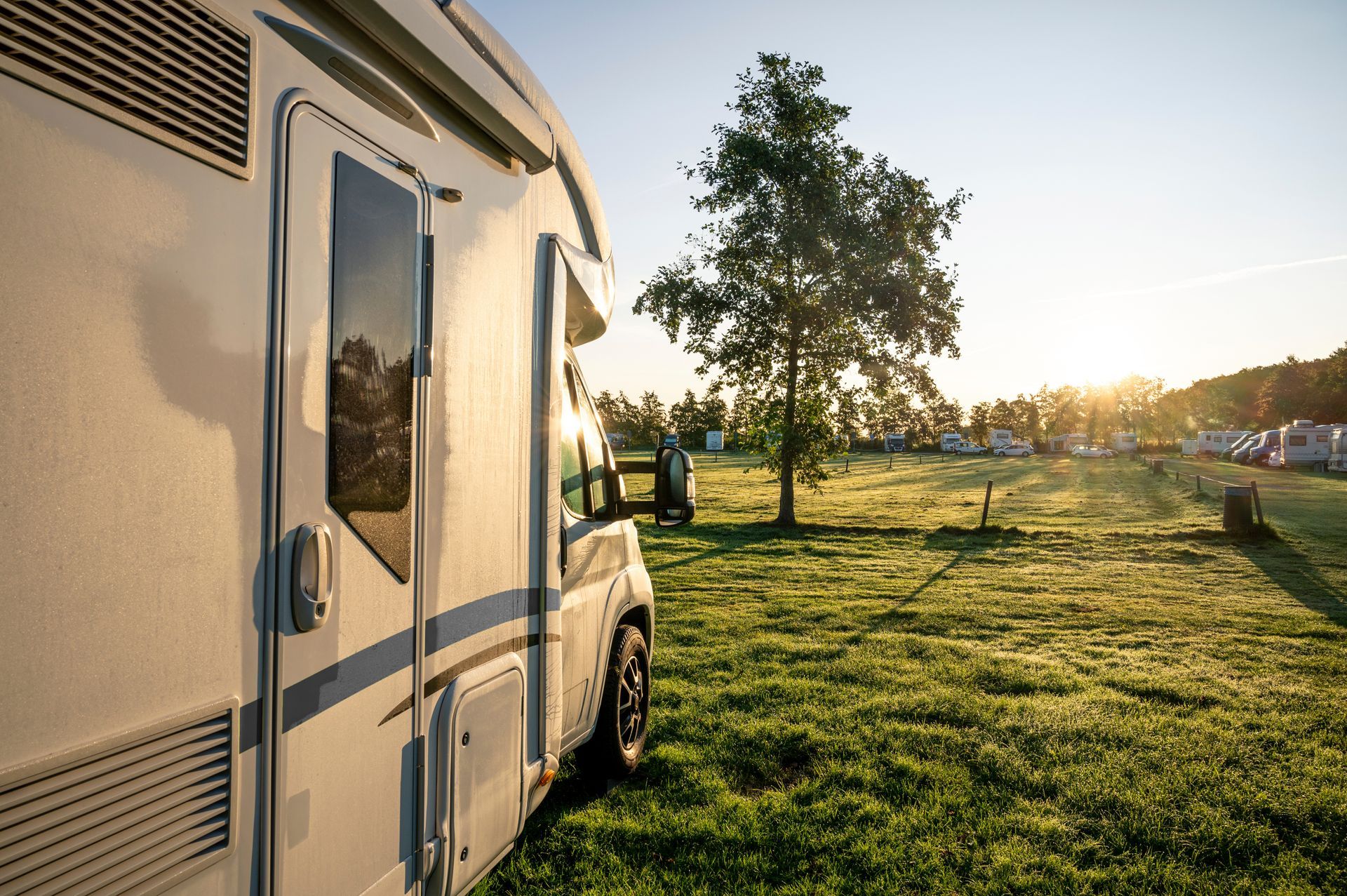 A rv is parked in a grassy field with a tree in the background.