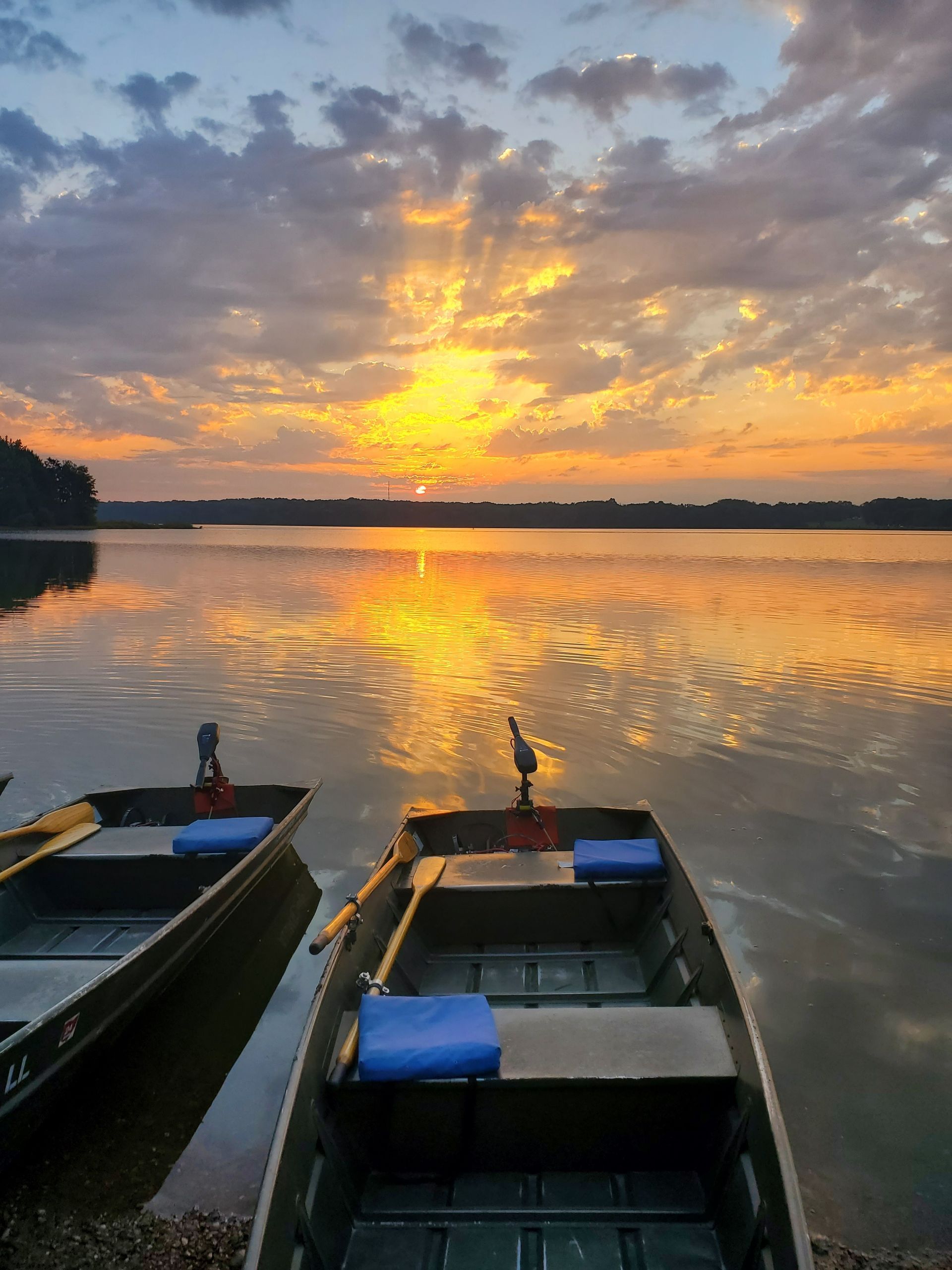 Two boats are sitting on the shore of a lake at sunset.