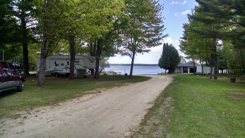 a dirt road leading to a lake with a rv parked on the side of it .