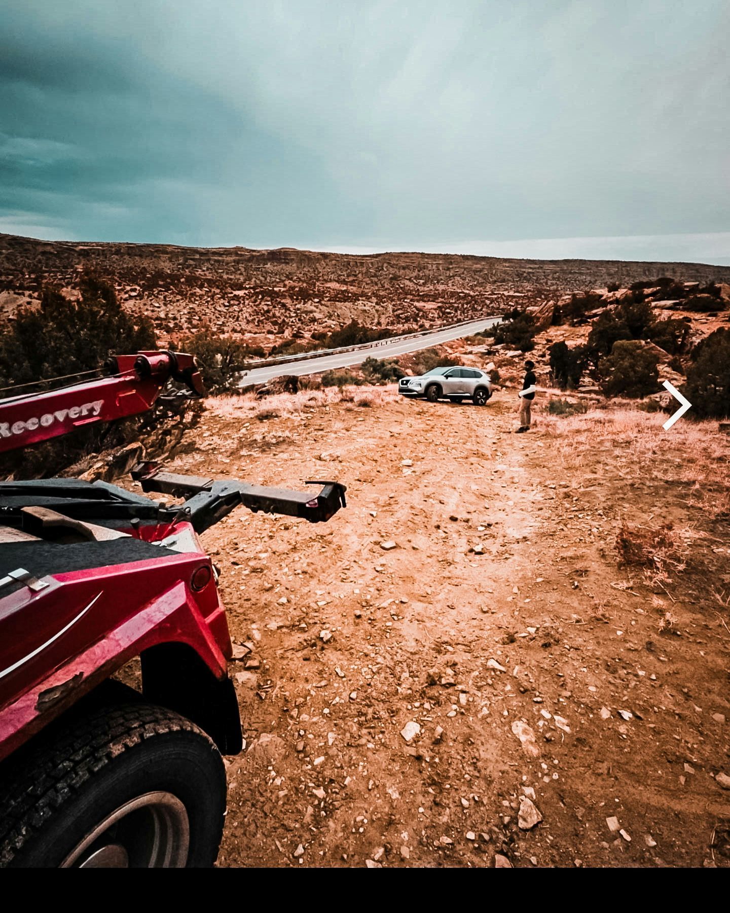 Red ATV and tow truck overlooking a desert landscape with a vehicle and person.