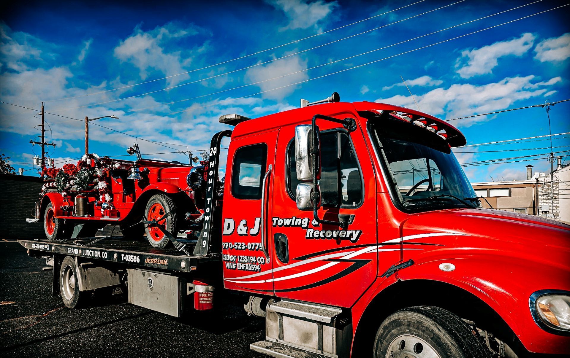 Red tow truck carrying a vintage red fire truck on a sunny day.
