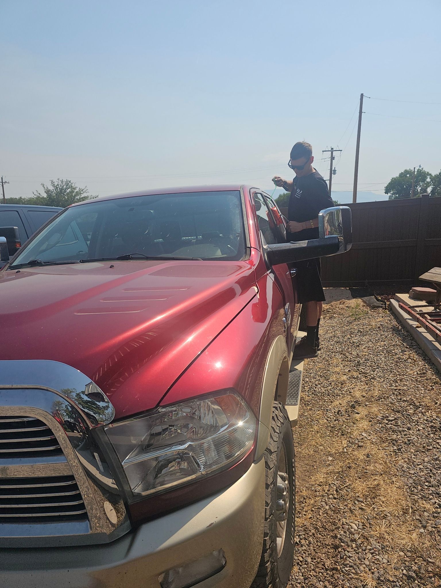 Red truck parked next to a person in a short-sleeved shirt outdoors. Sunny day.