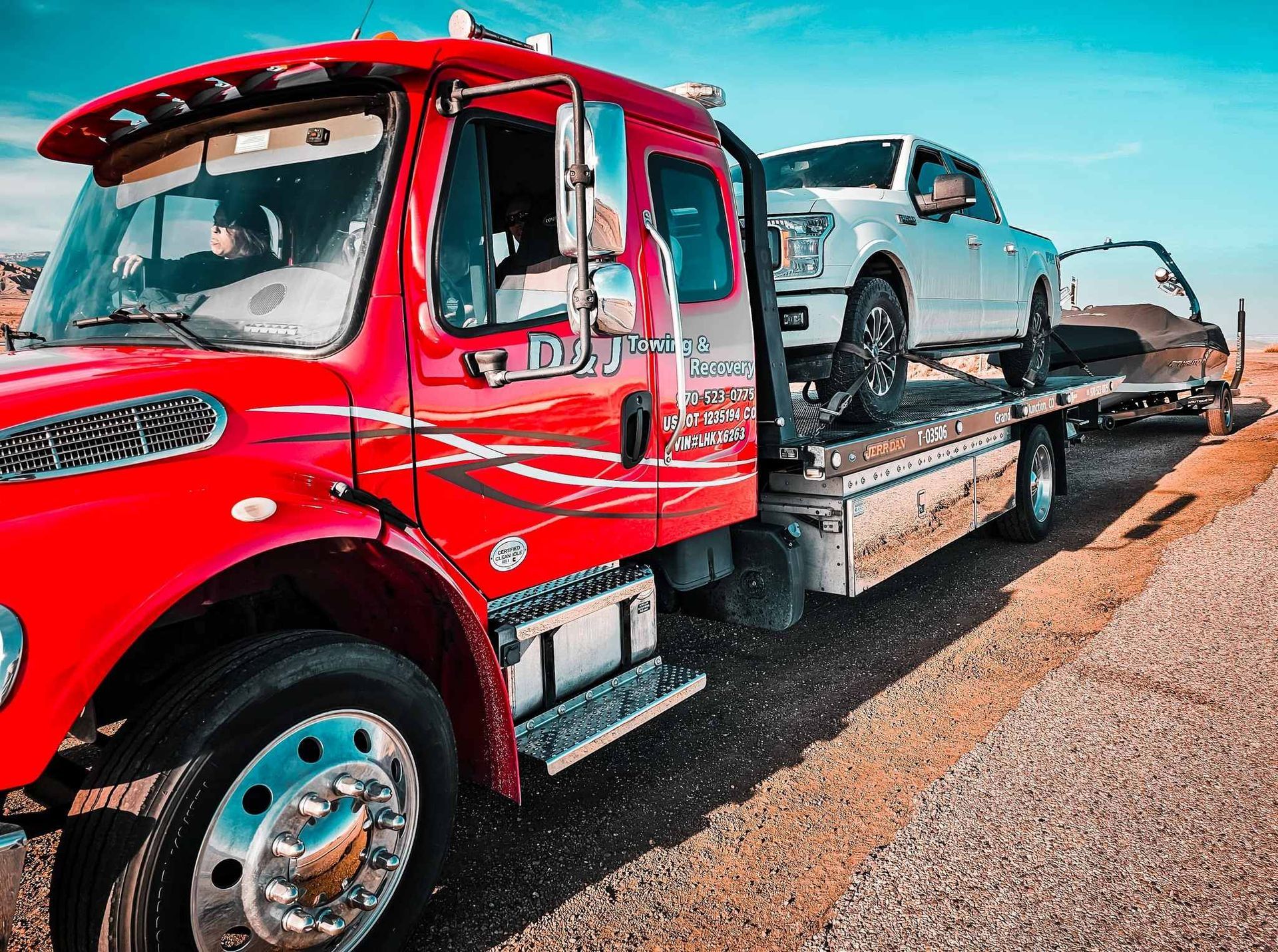Red tow truck carrying a white pickup truck and a black car on a sunny day.