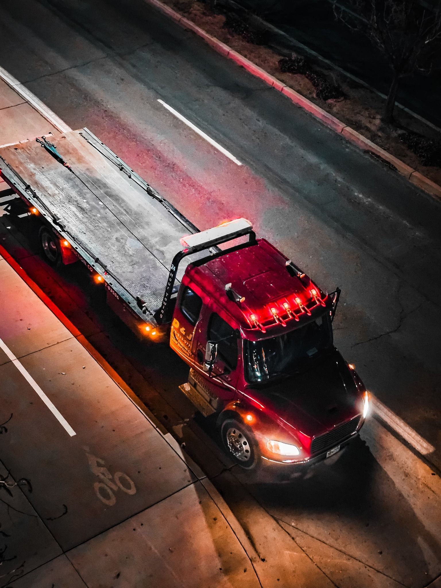 Red tow truck on a dark road with an empty flatbed. Nighttime scene, bright lights.