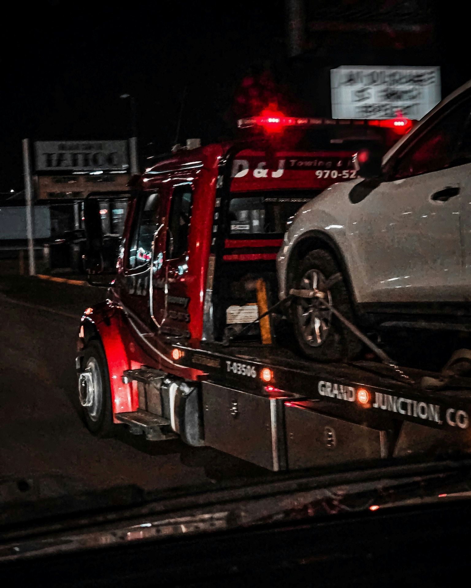 Red tow truck hauling a white SUV at night; red emergency lights on.