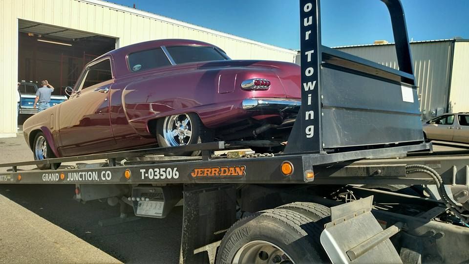 Burgundy classic car on a tow truck, under sunlight. 